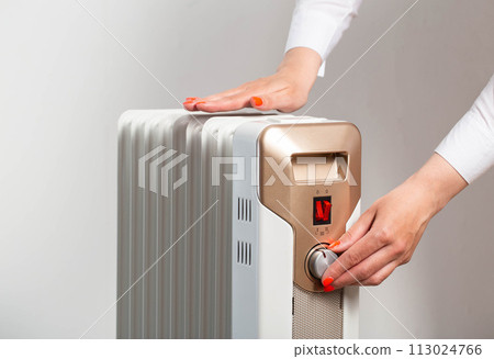 A woman's hand regulates the heating temperature on an electric heater, close-up 113024766