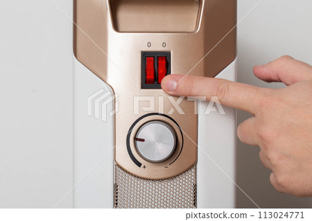 A man's hand turns on an electric heater, close-up. A man's hand turns on an electric heater, close-up. 113024771