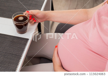 Pregnant girl drinks coffee from a cup. The benefits and harms of coffee for pregnant women, close-up 113024863