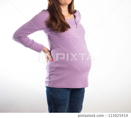 A pregnant girl in a purple sweater on a white background holds on to her back with back pain. The concept of chronic diseases in pregnant women osteochondrosis and intervertebral hernia. 113025419