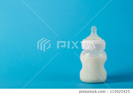 Baby bottle with milk for feeding babies on a blue background. Milk mixture enriched with bifidobacteria, vitamins and minerals. Copy space for text, healthy microbiota Baby bottle with milk for feeding babies on a blue background. Milk mixture enriched with bifidobacteria, vitamins and minerals. Copy space for text, healthy microbiota 113025425