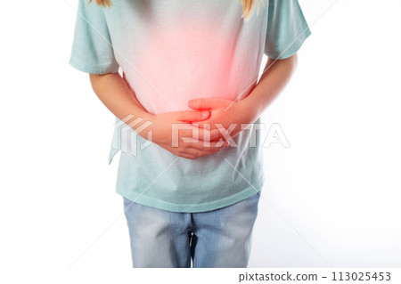 A seven-year-old girl in a green T-shirt holds her inflamed red stomach with her hands on a white background, isolate. Disease concept with colic and abdominal cramps, appendicitis in children. 113025453