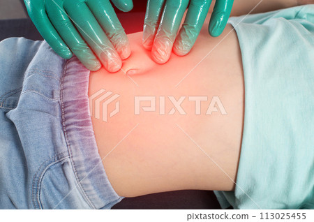 A surgeon doctor palpates the abdomen of the peri-umbilical zone during an abdominal hernia in a little girl. The concept of an extended umbilical ring, abdominal tension, umbilical hernia in 113025455