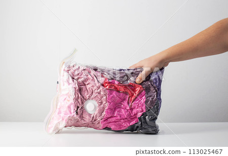 A man's hand holds sealed bags with vacuum-sealed clothes for storage on a white background. Copy space for text A man's hand holds sealed bags with vacuum-sealed clothes for storage on a white background. Copy space for text 113025467