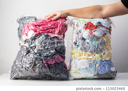 A man's hand holds sealed bags with vacuum-sealed clothes for storage on a white background 113025468