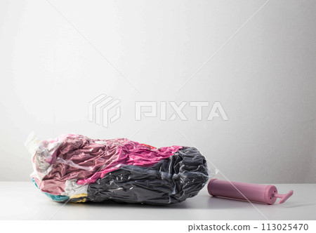 Pink hand pump for pumping air out of a bag with things on a white background. Modern technology for compact storage of things and clothes. Copy space for text 113025470