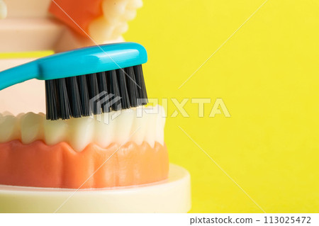 Blue toothbrush with charcoal coating near a mock-up of a dental jaw on a yellow background. Oral care and dental hygiene concept. Prevention of caries, close-up. Copy space for text 113025472