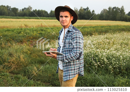 A farmer amidst a verdant wheat field, holding a tablet, symbolizing smart farming. Agronomist backdrop 113025810