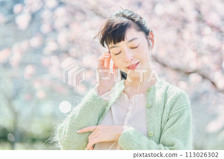 A woman listening to music among cherry blossoms A woman listening to music among cherry blossoms 113026302