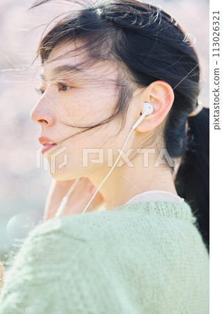 A woman listening to music among cherry blossoms A woman listening to music among cherry blossoms 113026321