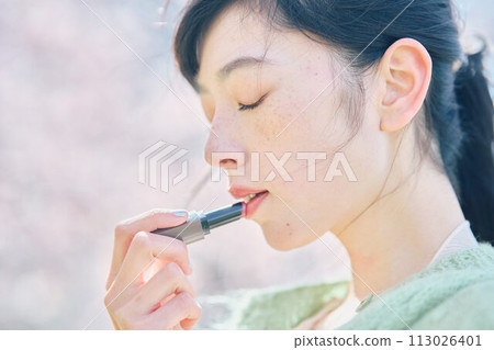A woman applying lipstick in cherry blossoms A woman applying lipstick in cherry blossoms 113026401