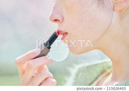 A woman applying lipstick in cherry blossoms A woman applying lipstick in cherry blossoms 113026405