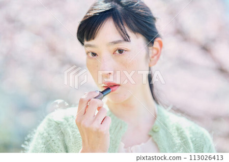 A woman applying lipstick in cherry blossoms A woman applying lipstick in cherry blossoms 113026413