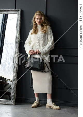 Studio portrait of beautiful woman with a curly blond hair holding black bag, posing on gray background. 113026601