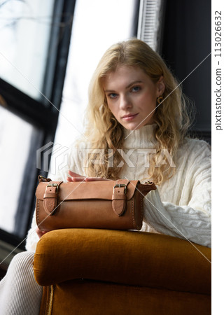 beautiful curly blond hair woman posing with a small tube brown bag in a vintage chair 113026632