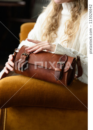 beautiful curly blond hair woman posing with a small tube brown bag in a vintage chair beautiful curly blond hair woman posing with a small tube brown bag in a vintage chair 113026642