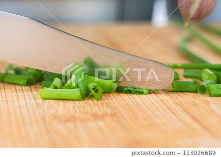 Chopped pieces of green chives and metal knife on wooden board, macro view Chopped pieces of green chives and metal knife on wooden board, macro view 113026689