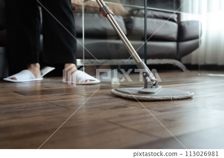 Housewife mopping parquet floor in living room. Hygiene and housekeeping concept 113026981
