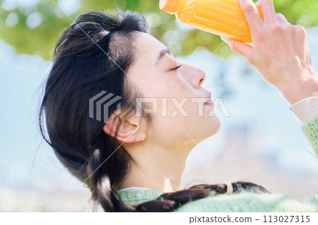 A woman drinking orange juice in a fresh green park 113027315