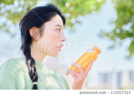 A woman drinking orange juice in a fresh green park 113027323
