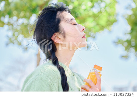 A woman drinking orange juice in a fresh green park 113027324
