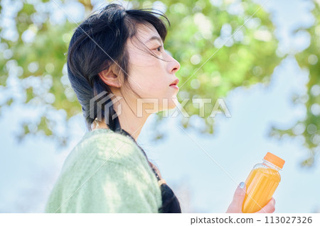 一個女人在新鮮的綠色公園裡喝著柳橙汁 113027326