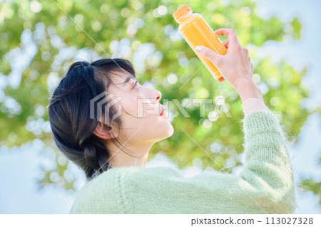A woman drinking orange juice in a fresh green park A woman drinking orange juice in a fresh green park 113027328