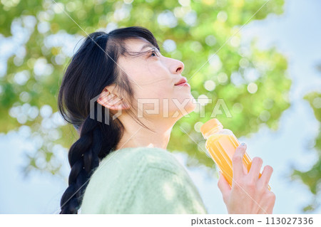一個女人在新鮮的綠色公園裡喝著柳橙汁 113027336