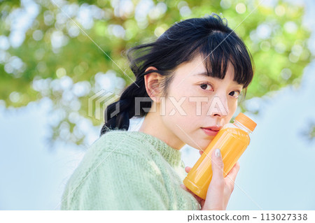 一個女人在新鮮的綠色公園裡喝著柳橙汁 113027338