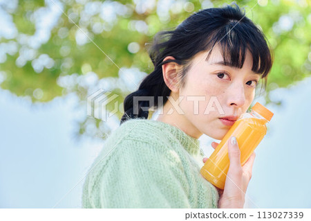 一個女人在新鮮的綠色公園裡喝著柳橙汁 113027339