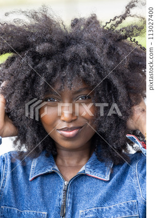 Vibrant Woman Smiling with Playful Afro Hairstyle in Denim Attire 113027400