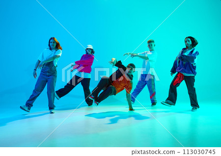 Group of streetstyle dancers energetically moves in sync in neon light against gradient colorful studio background. Group of streetstyle dancers energetically moves in sync in neon light against gradient colorful studio background. 113030745