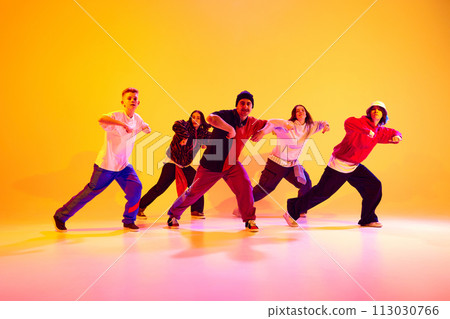 Energetic dance team performing contemporary dance moves in neon light against gradient colorful studio background. 113030766