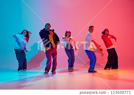 Modern dance crew in synch motion performing hip-hop in neon light against gradient colorful studio background. Modern dance crew in synch motion performing hip-hop in neon light against gradient colorful studio background. 113030771