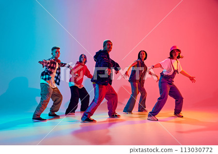 Energetic young dancers in street fashion clothes dance in neon light against gradient colorful studio background. Energetic young dancers in street fashion clothes dance in neon light against gradient colorful studio background. 113030772