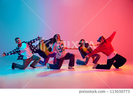 Dynamic squad of young dancers performing their routine in neon light against gradient colorful studio background. Dynamic squad of young dancers performing their routine in neon light against gradient colorful studio background. 113030773
