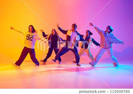 Dynamic portrait of young dancer in streetstyle clothes dancing in neon light against gradient colorful studio background. Dynamic portrait of young dancer in streetstyle clothes dancing in neon light against gradient colorful studio background. 113030780