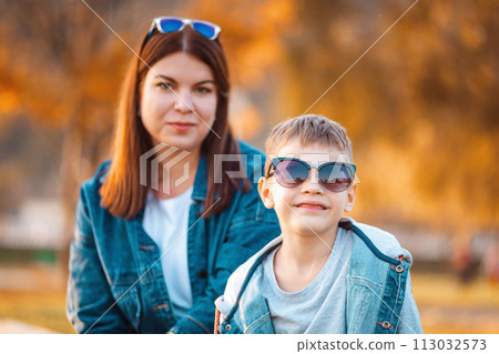 Portrait of young smiling mother and her son. In the background is autumn park. The concept of a happy childhood 113032573