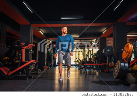 A young muscular athletic man walks through the gym. Low angle view. The concept of sports and fitness A young muscular athletic man walks through the gym. Low angle view. The concept of sports and fitness 113032653