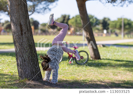 A girl is doing a handstand on a tree trunk in a park 113033525