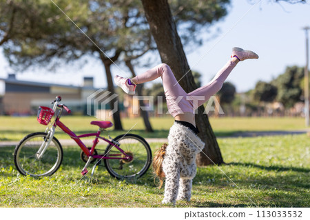 A girl is doing a handstand in the grass next to a bicycle 113033532