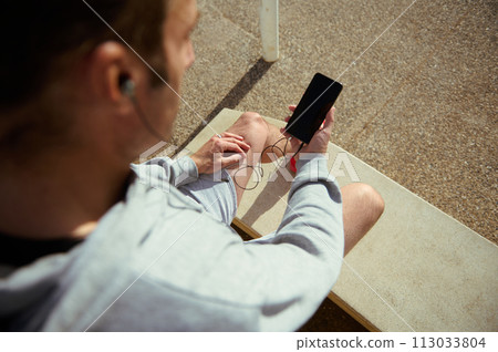 Overhead view of young man using mobile phone with blank black mockup screen, copy advertising space mobile app. Male athlete checking fitness application, heart rate while taking break during workout 113033804