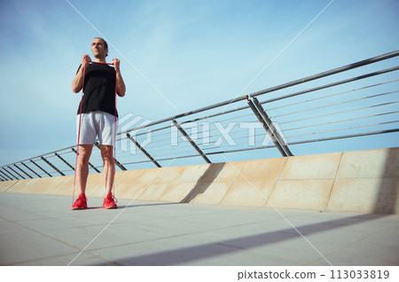 Full length portrait of active young man with athletic body performs bodyweight fitness exercises using a resistance band. Male athlete working out outdoors. Strength and motivation. Copy ad space 113033819