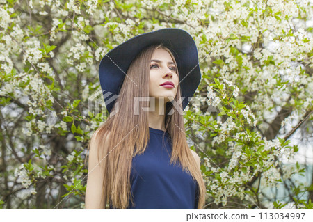 Cute fashion model with long brown hair and natural makeup against floral background outdoor 113034997