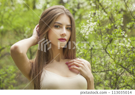 Posing young woman with natural makeup and healthy long brown hair in blossom park outdoors. Posing young woman with natural makeup and healthy long brown hair in blossom park outdoors. 113035014