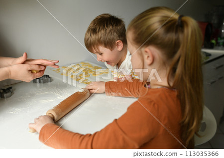 Brother and sister rolling out bunny cookie dough for Easter 113035366
