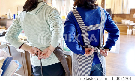 Rear view of two women tying their aprons behind_wide Rear view of two women tying their aprons behind_wide 113035701