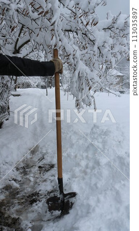 A man with a shovel standing behind the scenes after clearing snow in the garden, vertical shot, clearing snowdrifts from a backyard path with a shovel after a heavy snow storm 113035897