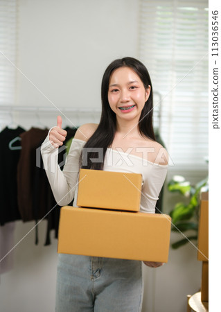 Asian business woman thumbs up working at home preparing SME package boxes for delivery at small business home office. 113036546