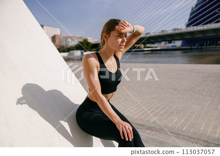 Young female athlete in sportswear have a rest after morning jogging outside and looks away 113037057